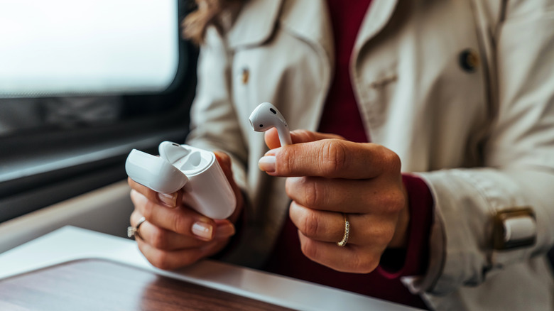 Woman holding one AirPod in one hand and charging case in the other