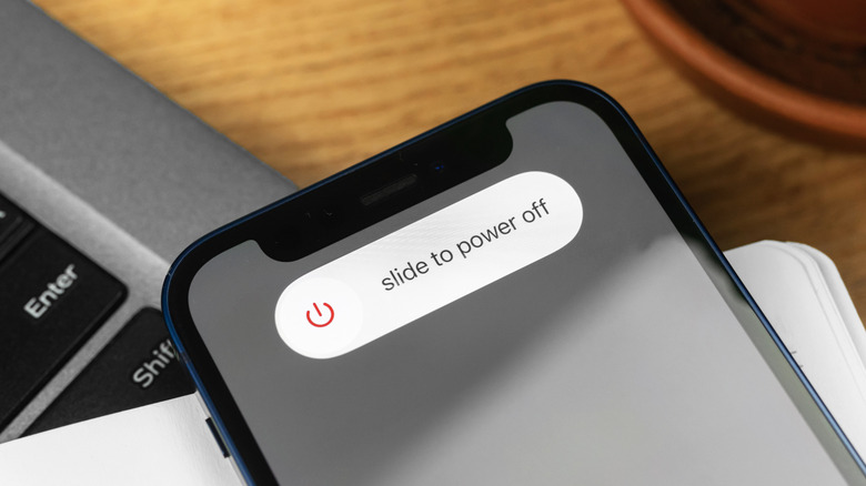 An iPhone laying on top of a notepad and MacBook, with the iPhone displaying the shut down screen