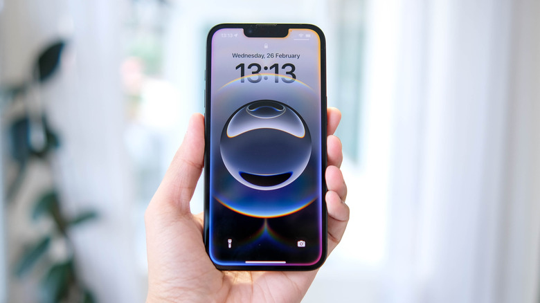 A hand holding an iPhone while the device displays the Lock Screen