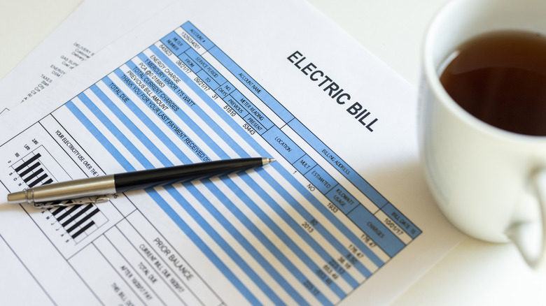 An electric bill on a table with a cup of coffee next to it