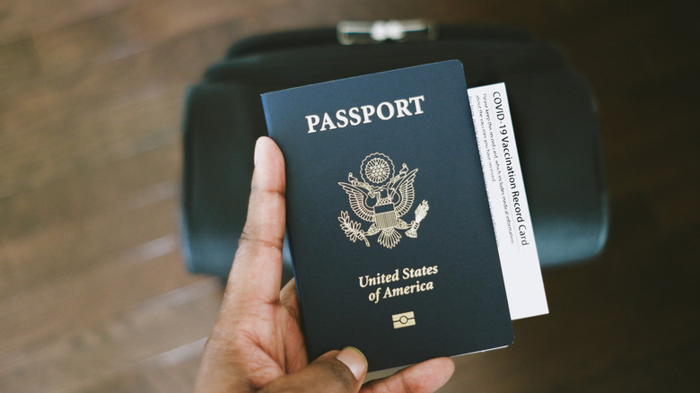a hand holding a US passport ID with a suitcase in the background