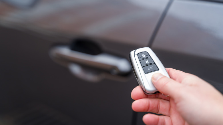 A hand holding a key fob up to a car.