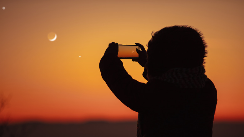 A person taking a photo of the moon with a smartphone.
