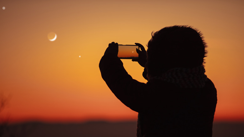 A person taking a photo of the moon with a smartphone.