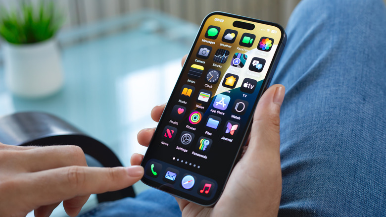 A seated individual pointing at the Phone app button on their iPhone Home screen