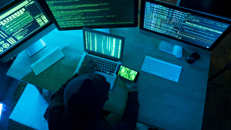 Hacker with multiple monitors and a mobile phone