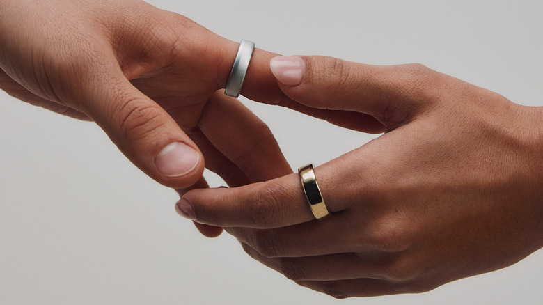 Two hands linked wearing silver and gold Oura Rings.