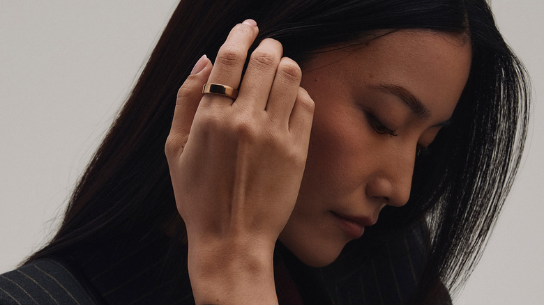 A side profile of a woman with a rose gold Oura Ring on her hand, held up by her head.