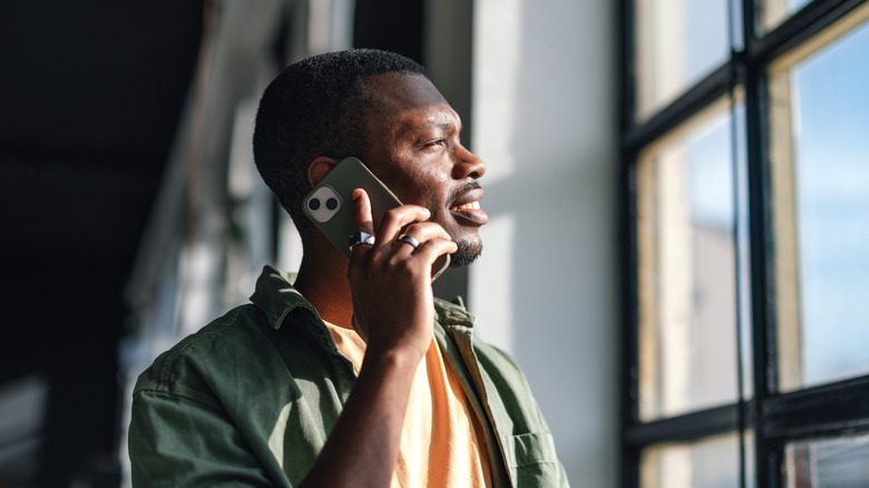 a man holds a cell phone while looking out a window