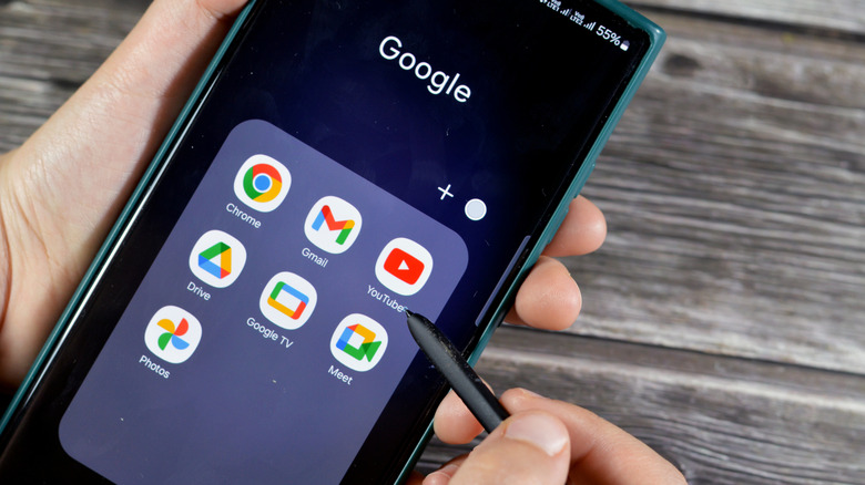 Smartphone display with Google apps visible and hand holding stylus.