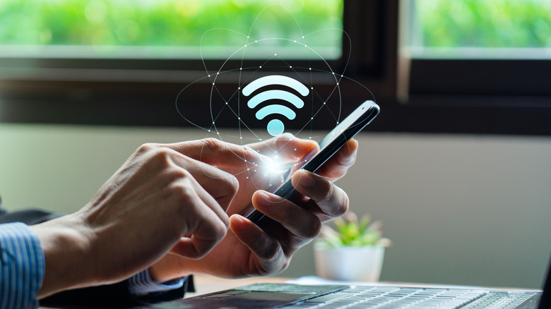 A person holding a phone near a laptop with the Wi-Fi symbol shining above it