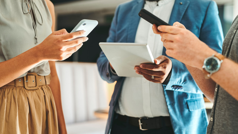 Three people holding two phones and a tablet next to each other