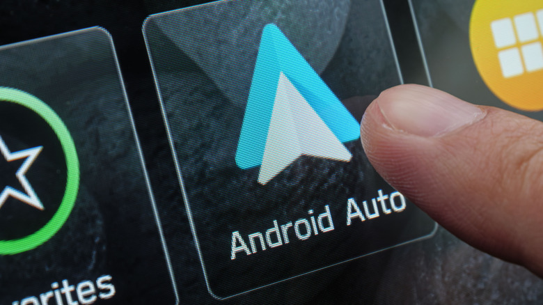 A finger touching the Android Auto button on a car's dash head unit.