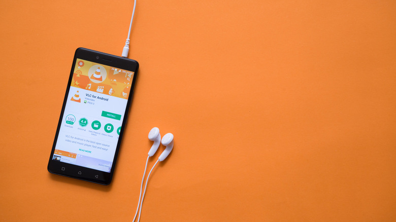 An old phone connected to earphones showing VLC in the Play Store