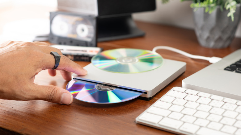Hand putting disc into disc drive connected to computer