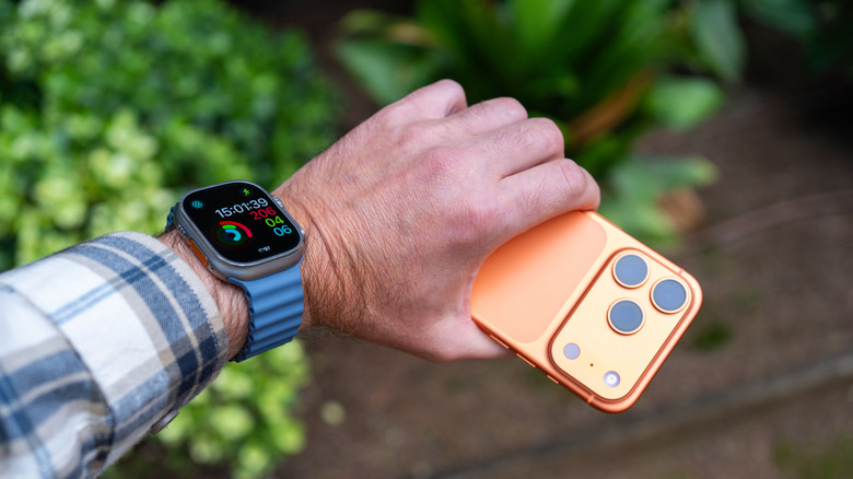 A man's hand holding an orange iPhone with an Apple Watch on his wrist.