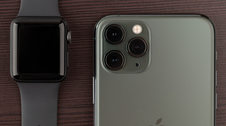 An Apple Watch beside an iPhone on a wood table.