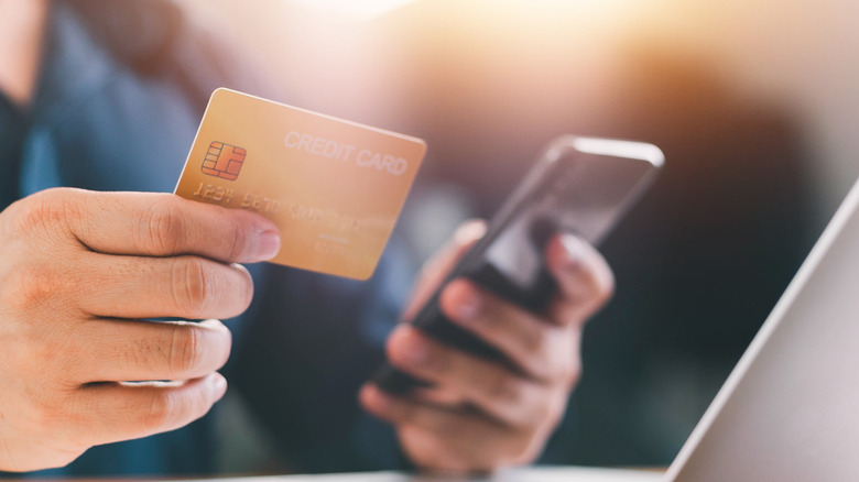 A person holding a credit card in one hand and their phone in the other
