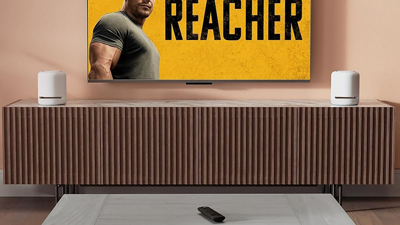 Un control remoto de Amazon Fire TV Stick sobre una mesa con un televisor frente a él.