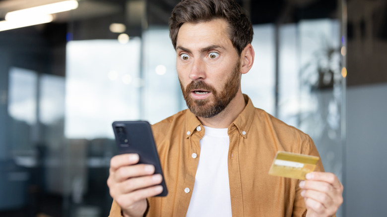 a man holding his credit card and looking at his phone in shock because his information was stolen