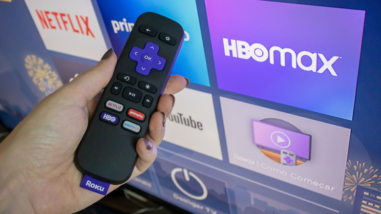 Roku remote in front of Roku interface on TV with app channels in view.