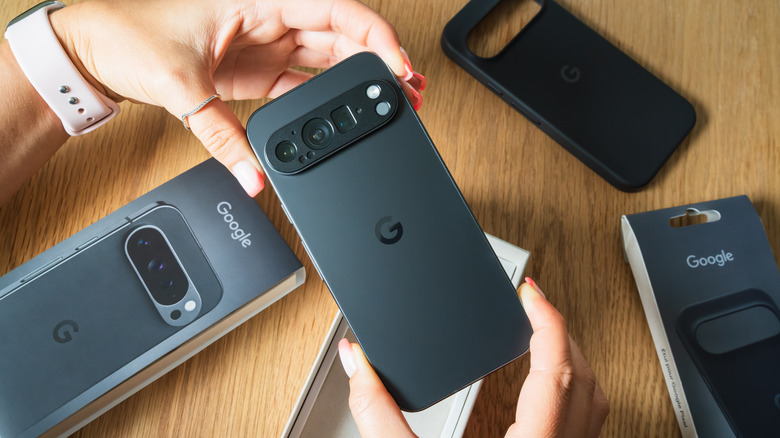 Person holding a Google Pixel phone in both hands with accessories on the table behind it