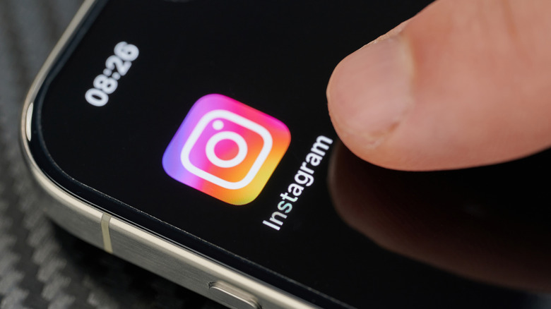 A finger pointing at the Instagram icon on an iPhone 15 Pro screen