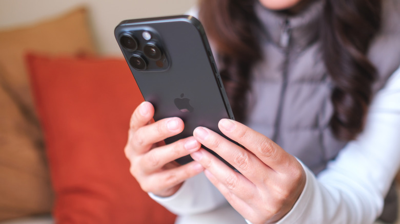 A closeup of a woman holding a black iPhone 15 Pro Max in both hands