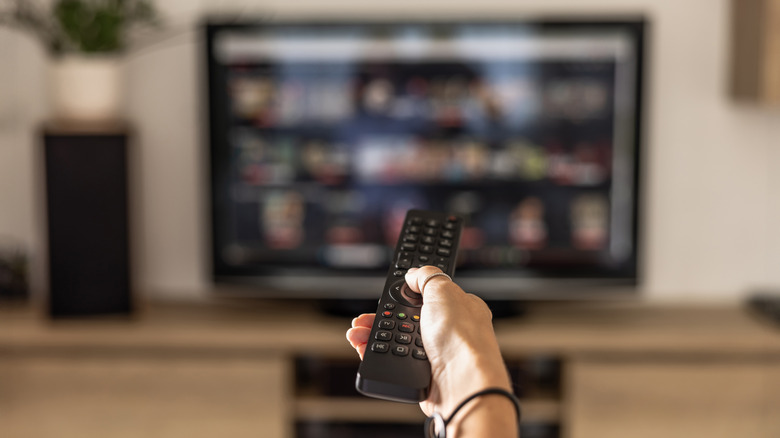 Person holding up remote browsing TV streaming service out of focus