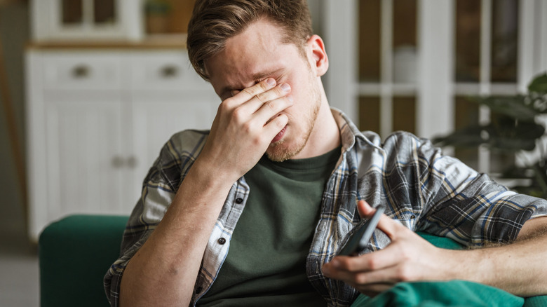 a man rubbing at his eyes while holding his smartphone