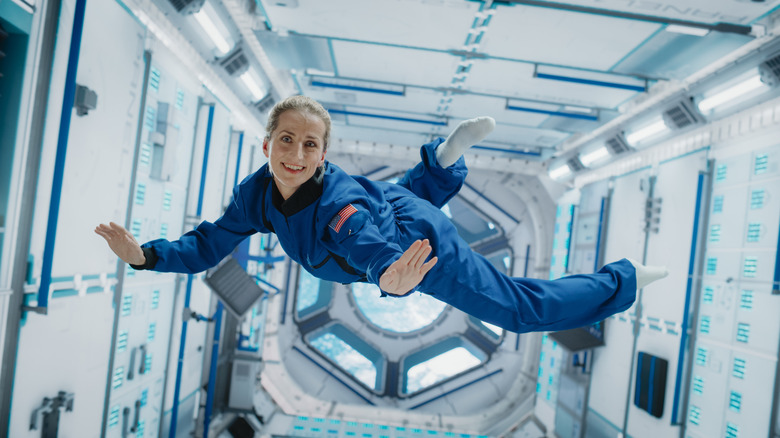 Astronaut wearing blue jumpsuit floating in space station