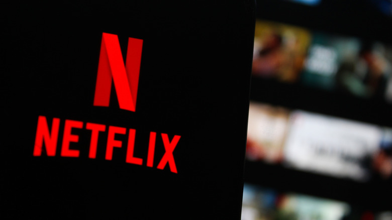 Netflix logo on a smartphone with the desktop UI in the background.