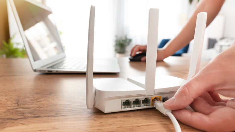 Person plugging in ethernet into Wi-Fi router with laptop on desk