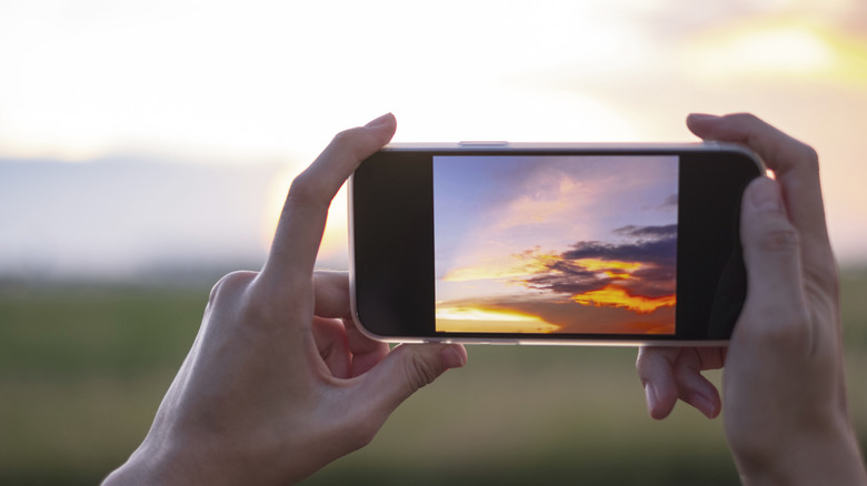 A person recording video of a sunset with a smartphone.