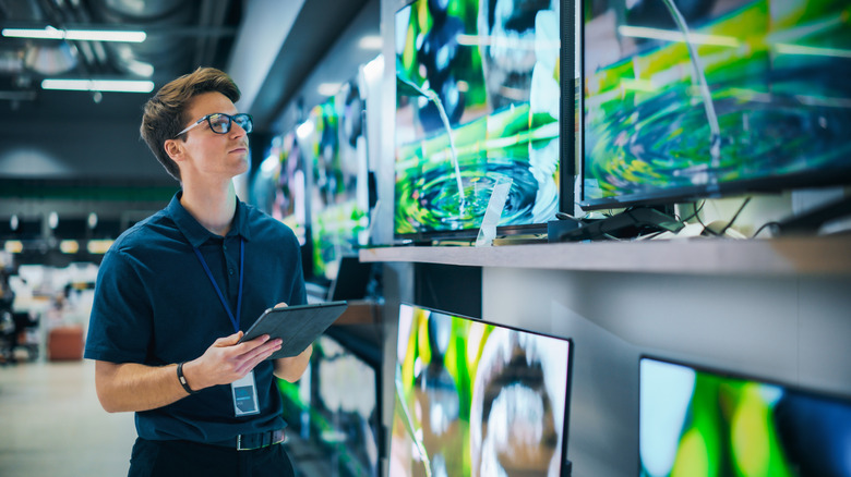 Store salesman inspecting and reviewing smart TVs on a retail store shelf.