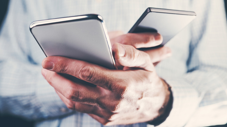 A man's hands holding two phones.