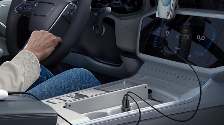 The Anker 30W 2-Port PowerIQ adapter connected to the 12V port of a car's center console. A wire runs from its to a vent-mounted smartphone.