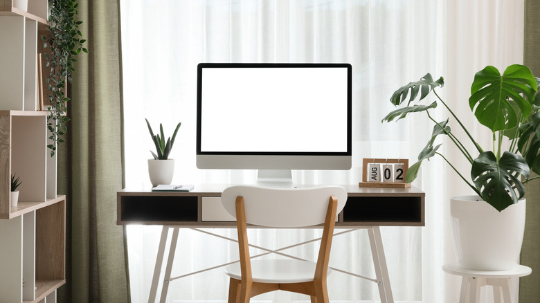 A computer monitor on a table in a room with a large window behind it.