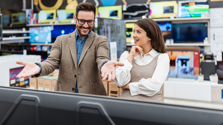 A man and woman reacting to a TV at an electronics store
