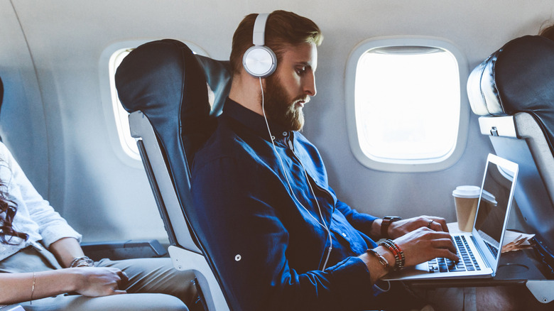 A man wearing headphones while using a computer aboard a flight