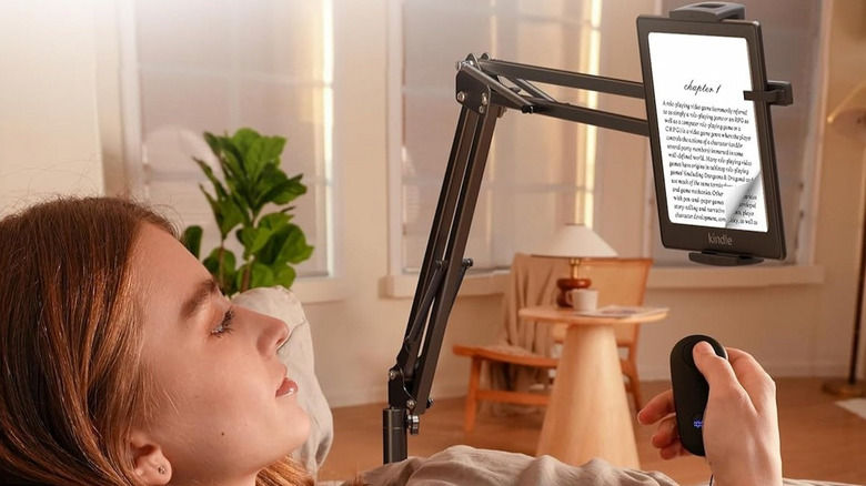 A woman lies on a sofa reading a Kindle that's mounted on the VoltifyMax Kindle holder