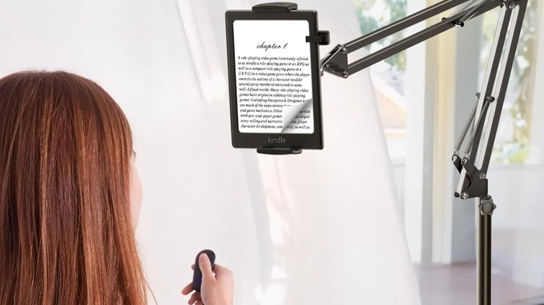 Back-of-head view of a woman using the VoltifyMax's remote to turn the page on her Kindle, mounted on the VoltifyMax Floor Stand