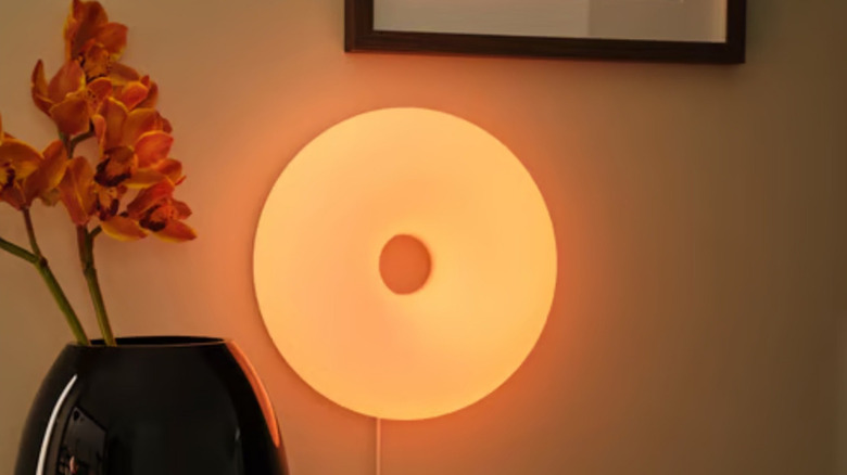 The VARMBLIXT dimmable LED lamp is wall-mounted and set to an orange color.
