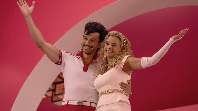 A smiling man and woman dressed in retro-style clothing wave enthusiastically