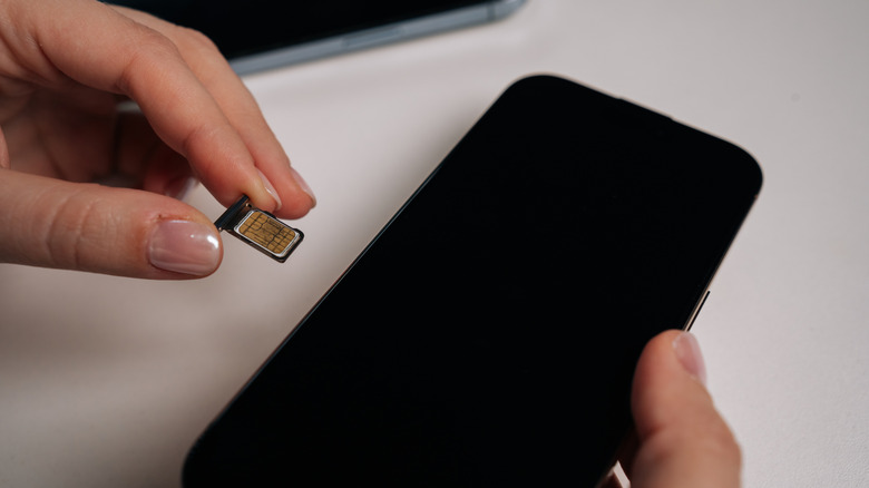 person holding sim card next to smartphone, preparing to install