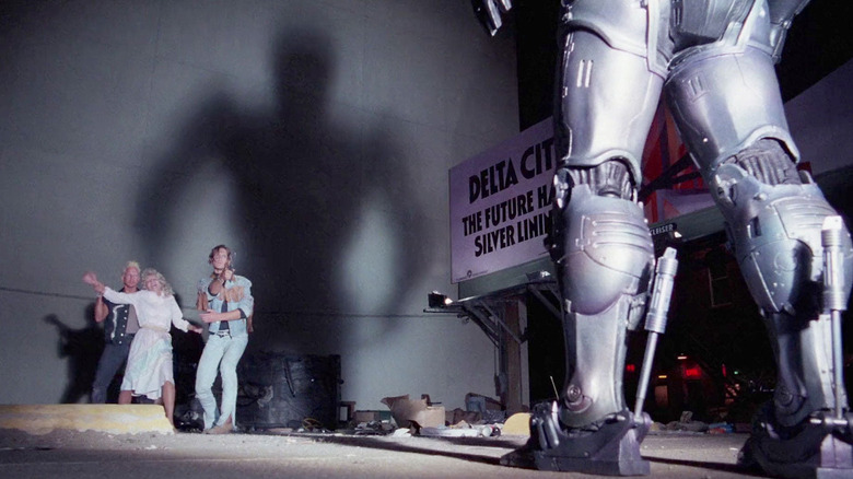 RoboCop casting a shadow on a wall as criminals hold a hostage