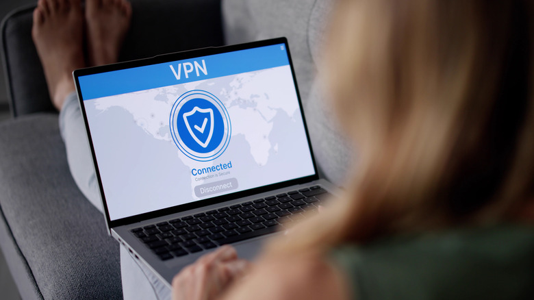 person lying on a sofa holding a laptop with a VPN connection screen