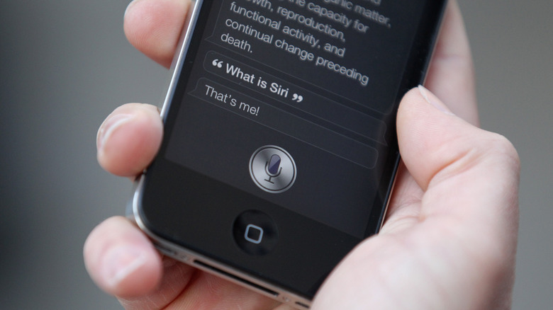 A person's hand holding an iPhone displaying the Siri functionality