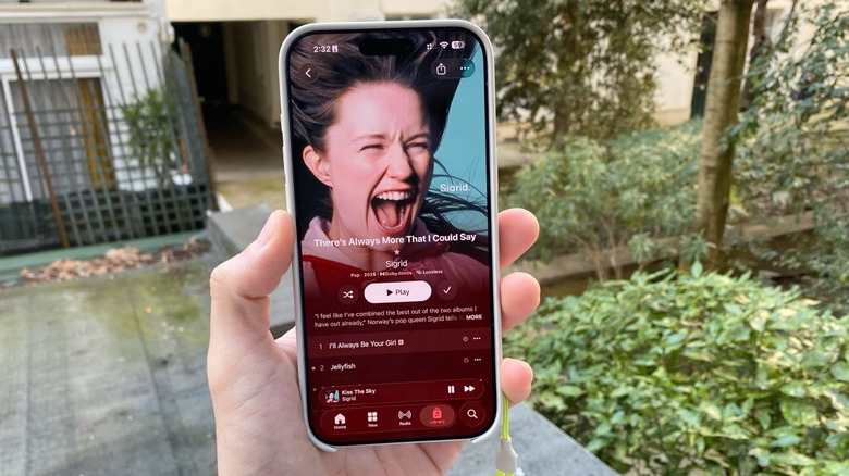 A hand holding an iPhone 17 Pro Max. On the display, Apple Music's new full album background.