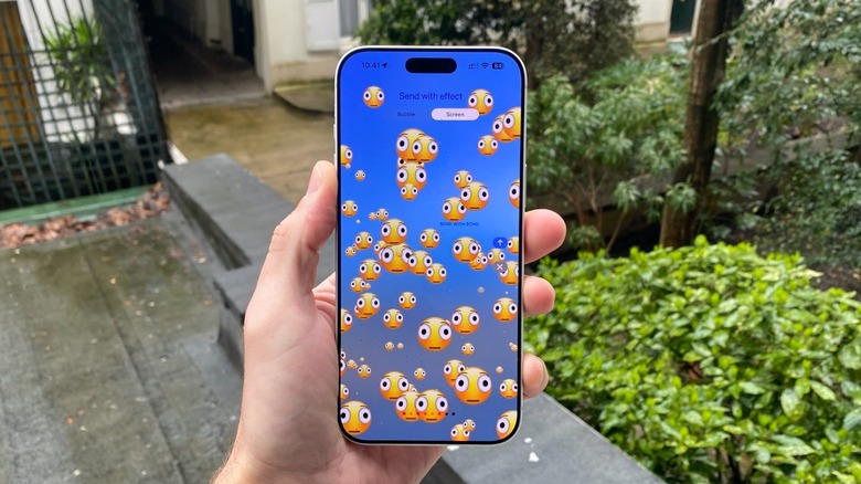 A hand holding an iPhone 17 Pro Max. On the display, several distorted face emojis.